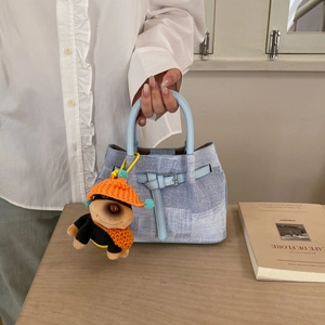 Close-up of light blue textured handbag featuring a cute plush dog keychain and metal buckle