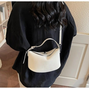 Detail of minimalist cream half-moon bucket bag featuring a sleek handle and thin shoulder strap