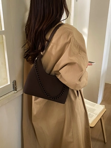 Detail view of dark brown pebbled leather texture and thick chain on a shoulder bag