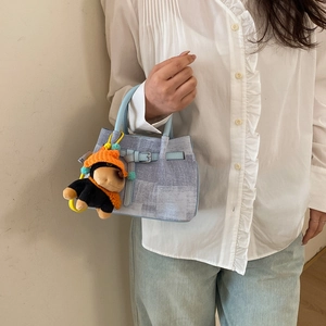 Detail of light blue denim texture handbag with a cute puppy plush charm and silver buckle