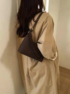 Detail of dark brown litchi pattern leather handbag with chain on beige trench coat