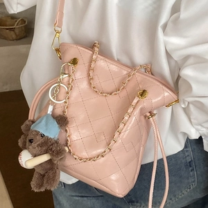 Pink quilted bucket bag with gold chain and bear charm shown on a female model