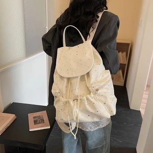 Detail of white drawstring backpack featuring silver star patterns and flap closure