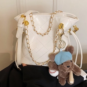 White quilted bucket bag with gold chain strap and cute bear pendant on black fabric