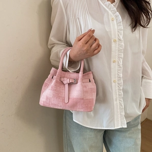 Detailed view of pink textured bucket bag with leather handle on casual outfit
