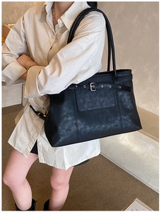 Close-up of black textured faux leather tote bag with metal buckle and shoulder strap