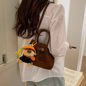 Brown matte leather bucket bag with cute puppy charm worn by a model in a warm room