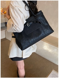 Detail of a large black tote bag with silver buckle and straps shown on a model's shoulder