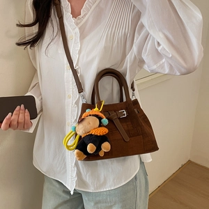 Detail of vintage brown suede handbag featuring a cute plush gorilla charm and leather strap
