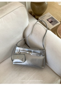 Detail der silbernen Metallic-Tasche mit abnehmbarem Portemonnaie auf beigem Sofa