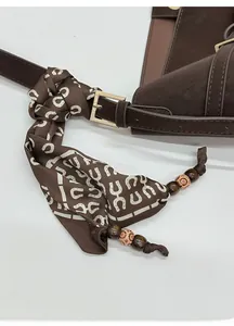 Détail rapproché du sac en cuir marron café avec foulard en soie décoratif et boucle dorée