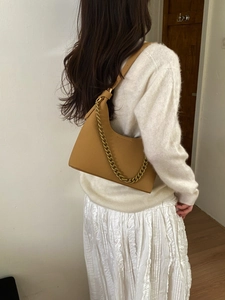 Close-up of ginger leather hobo bag with gold chain strap on a model outfit