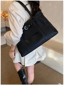 Detailed view of black leather tote bag featuring silver metal buckle on spacious front pocket