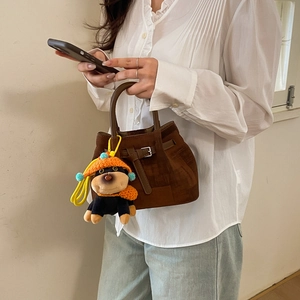 Detail view of brown suede bucket bag with a cute plush dog charm wearing an orange hat