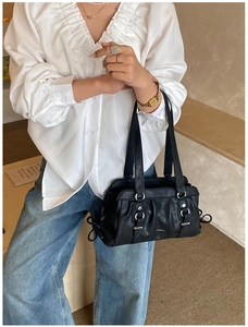 Close-up of black pleated PU leather shoulder bag with silver buckles and drawstring details