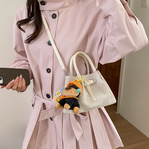 Close-up of stylish mini beige bucket bag with cute black puppy charm on pink coat