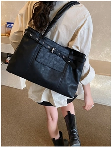 Detail of black leather tote bag with decorative belt buckle and metal eyelets