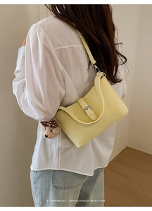 Detail of pale yellow retro shoulder bag with a cute plush bear charm on white shirt