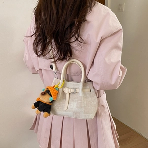 Detail of a beige bucket bag with a cute dog plush charm on a pink pleated coat