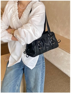 Detail view of black pleated leather underarm bag with side bow design on a model