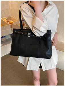 Detail of black matte leather tote bag featuring a silver metal buckle and strap on a model
