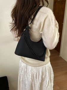 Close-up of black lychee grain leather handbag with matte chain strap and brand logo