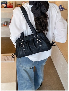 Detail of black pleated faux leather shoulder bag with silver rings and bow accents