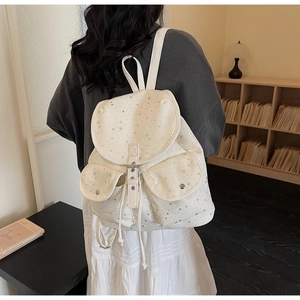 Close-up of white canvas backpack featuring silver star patterns and functional front pockets