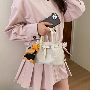 Detail of beige textured handbag featuring a cute plush dog charm and metal buckle