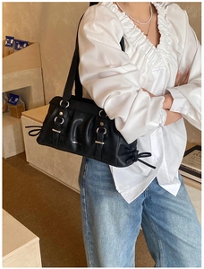 Detail of black pleated leather shoulder bag with silver rings and side bow decoration