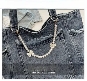 Detail of pearl bag chain with white bows and gold clasps on washed denim tote