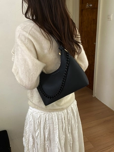 Close-up of black lychee grain leather underarm bag with bold chain detail on model