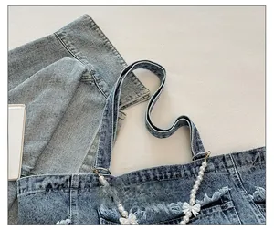 Close-up of washed denim tote bag featuring pearl bow chain and frayed edge details
