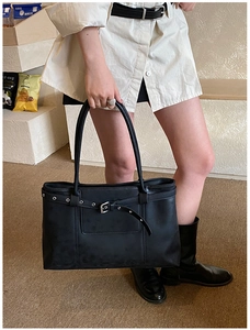 Macro view of black leather tote bag featuring buckle strap and silver metal eyelets
