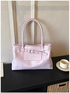 Detailed close-up of a pale pink tote bag with silver buckle on a wooden desk setup