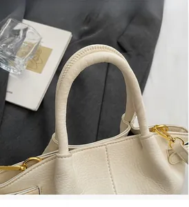Detaillierte Nahaufnahme der cremefarbenen Ledertasche mit robusten Griffen und Goldhaken