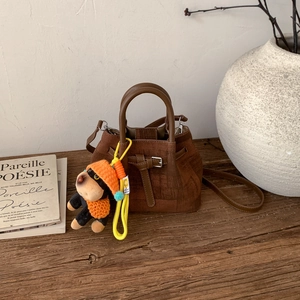 Brown suede crossbody bucket bag with dog pendant on a rustic wooden stand