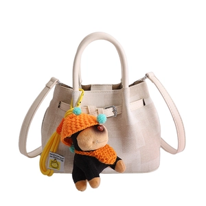 Minimalist beige textured fabric bucket bag with a cute plush monkey charm and leather strap