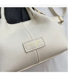 Detailaufnahme der weißen Handtasche mit Litschitextur, Goldlogo und feinen Ledernähten