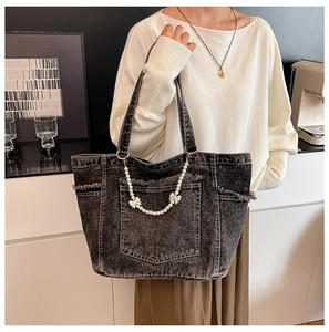 Detail of grey washed denim tote bag with decorative pearl and bow chain strap detail