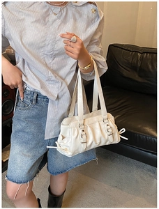 Close-up detail of white pleated shoulder bag featuring a silver metal buckle and side bow tie