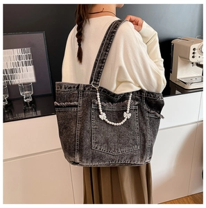 Detail of grey washed denim tote bag featuring raw edge pockets and pearl chain bow accessory