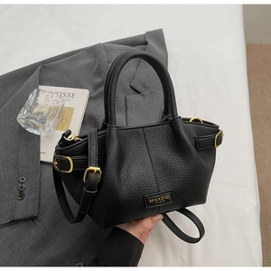 Detailansicht einer schwarzen Handtasche aus Leder mit Metalllogo und verstellbarem Riemen