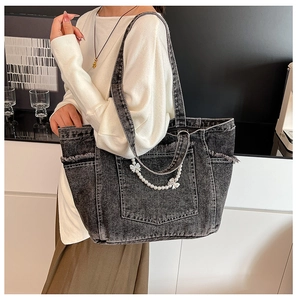 Detail of grey washed denim tote bag featuring white pearl chain and ribbon bow accents