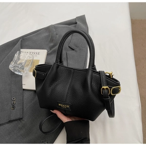 Detail einer schwarzen Handtasche aus Narbenleder mit goldener Hardware und Logo
