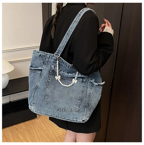 Detail of a washed denim tote bag with multi-pocket design and pearl bow accessory