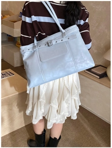 Close-up of light blue tote bag with metallic buckle and long handles in a lifestyle setting