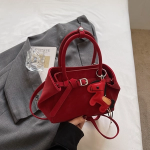 Elegante bolso bandolera de ante rojo con un colgante de caballo decorativo en cama