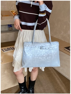 Close-up of glossy light blue tote bag with metallic buckle detail on fashion model