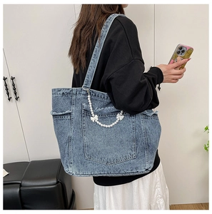Detail view of denim tote bag featuring fringe edges and elegant white pearl chain